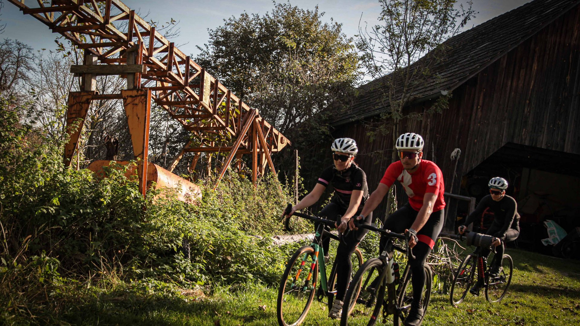 Gravel-Wundertüte Wörthersee © Wörthersee Tourismus GmbH - Christian Riedel Drei Radfahrer fahren auf einem grasbewachsenen Weg an einer alten Industrieanlage vorbei