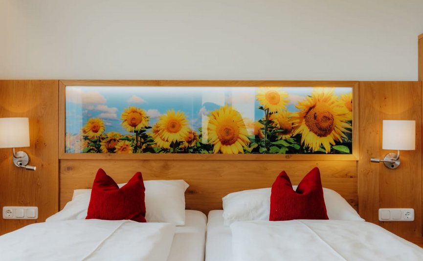 Goldener Herbst auf der Mühl4tler Alm Zwei Einzelbetten mit roten Kissen und Sonnenblumenbild an der Holzwand