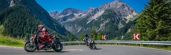 Motorradurlaub im Lechtal – Hahntennjoch © Moppetfoto.de Zwei Motorräder fahren eine Kurve in den Bergen mit blauem Himmel