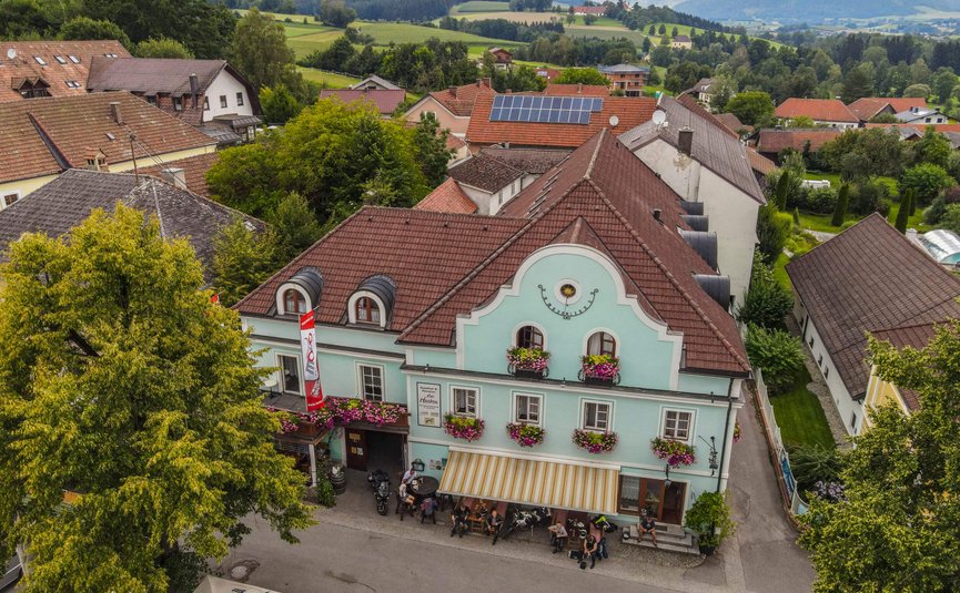 Altes Gasthaus mit blauen Fassade und Blumen in einem Dorf mit Bergen im Hintergrund
