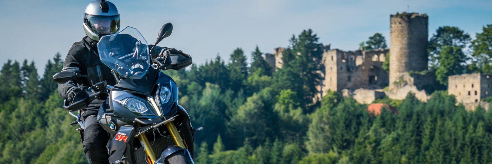Motorradfahrer auf Landstraße vor bewaldetem Hügel mit Burgruine