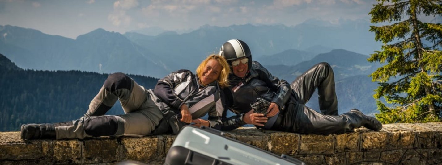 Special-Bike-Week Zwei Motorradfahrer lehnen entspannt auf einer Steinmauer mit Berglandschaft im Hintergrund