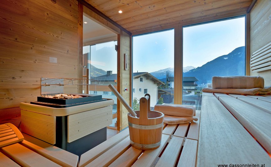 Sauna mit Holzbänken und Blick auf Berge und Häuser durch Glasfenster