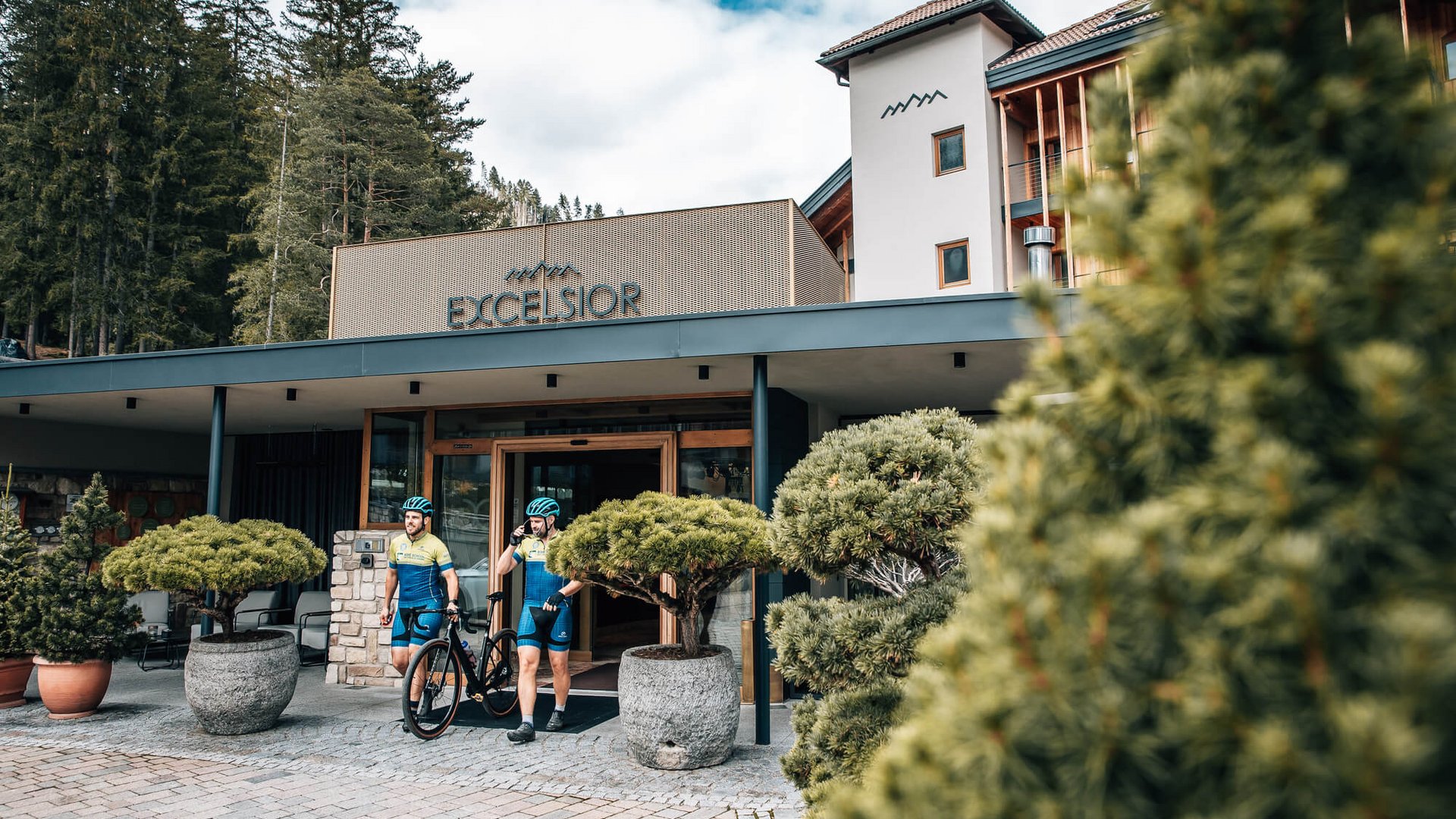 Prädikat: Außergewöhnlich © Jens Scheibe Zwei Radfahrer verlassen Hotel Excelsior in bewaldeter Berglandschaft