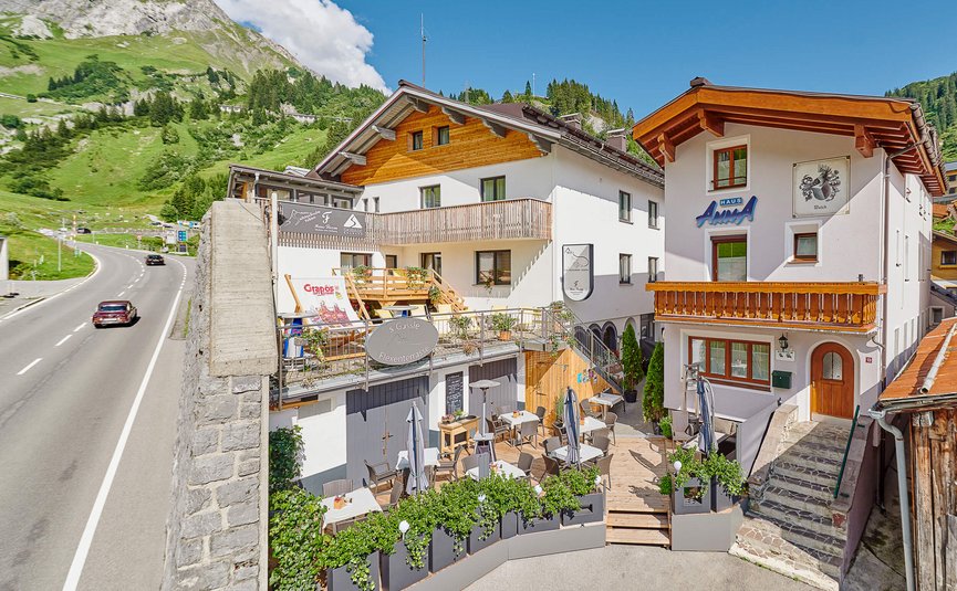Gastgarten mit Tischen und Stühlen vor Häusern in Alpenlandschaft