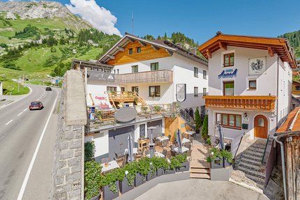 Haus Flexen © Mathies Wilhelm Robert jun. Gastgarten mit Tischen und Stühlen vor Häusern in Alpenlandschaft