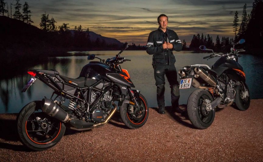 BIKEGENUSS "Großglockner" Zwei Motorräder stehen an einem See bei Sonnenuntergang, Mann in Motorradkleidung daneben