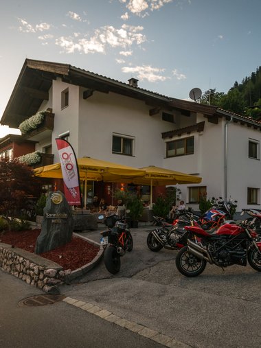 Motorradurlaub © Moppetfoto.de Hotel mit Motorrädern auf Parkplatz bei Sonnenuntergang in den Bergen