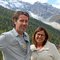 Ein Mann und eine Frau vor bewaldeten Bergen und schneebedecktem Gipfel