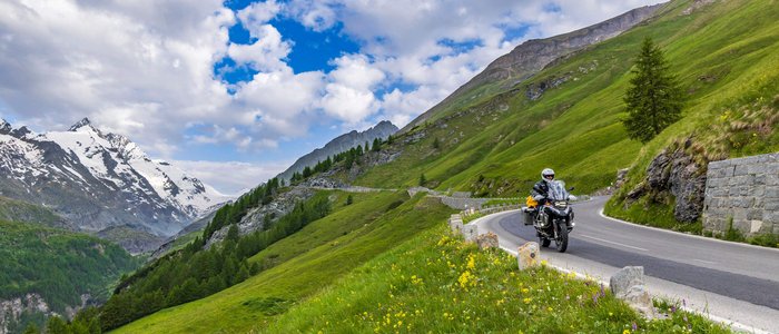 Erlebnishotel Kärnten-Mölltal ***S © Alexander Seger Motorradfahrer auf kurvenreicher Bergstraße mit grünen Wiesen und schneebedeckten Gipfeln