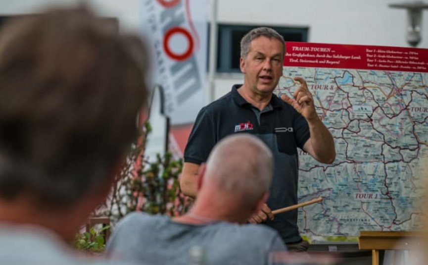 BIKEGENUSS "Großglockner" Mann erklärt Reiseroute auf Karte vor Publikum im Freien