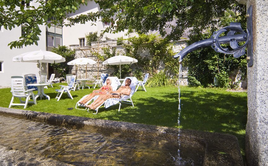 Hotel & Südtiroler Gasthaus Der Gassenwirt *** © Hotel Gassenwirt Paar sonnt sich auf Gartenliegen neben einem Wasserbrunnen
