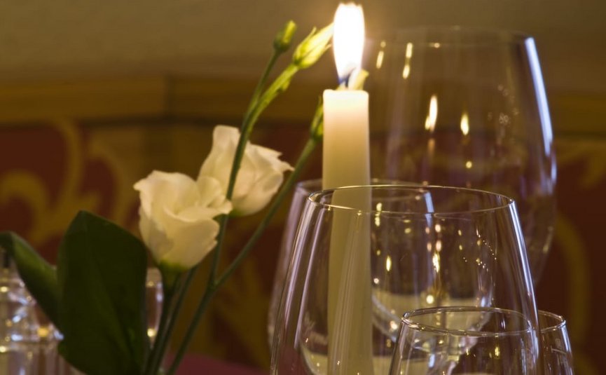 Brennende Kerze neben weißen Blumen und Weingläsern auf dem Tisch