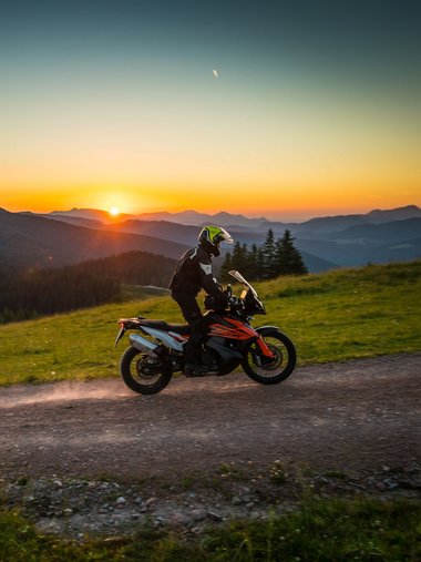 Motorradfahrer auf Schotterweg in den Bergen bei Sonnenuntergang