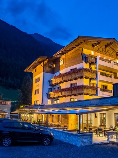 Beleuchtetes Hotel in den Bergen bei Nacht mit geparkten Autos