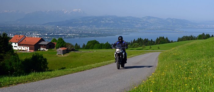 Allgäu © Hotel Bergblick Motorradfahrer auf Landstraße mit Alpenpanorama und See im Hintergrund