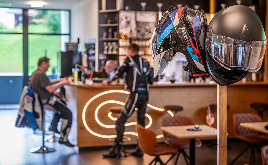 DAS UNTERRAIN lifestyle hotel **** © Armin Kleinlercher Motorradhelme an einem Ständer in einem Café mit Personen im Hintergrund