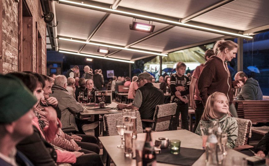 Menschen sitzen und unterhalten sich in einem überdachten Außenbereich eines Cafés abends
