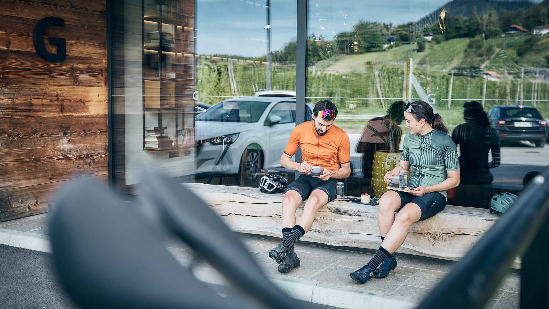 Zwei Radfahrer in Sportkleidung sitzen draußen und trinken Kaffee
