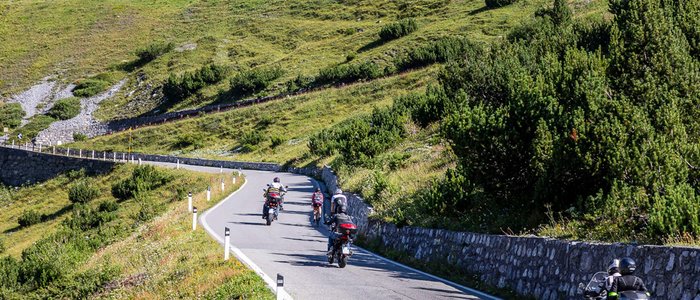 Motorradfahrer auf Bergstraße mit grünen Hängen und Graffiti an einer Mauer