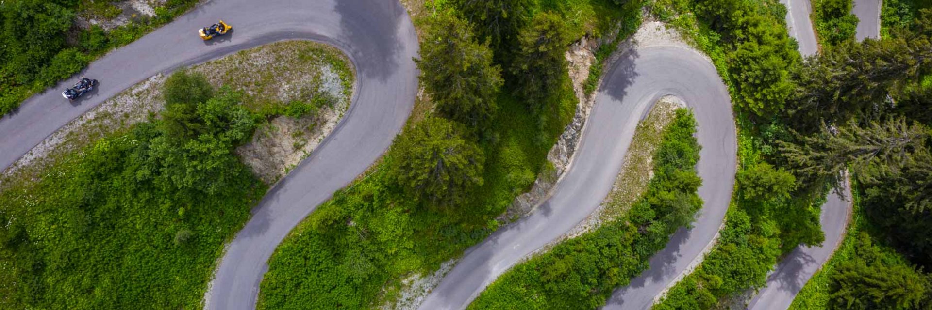 Paznaun – Silvretta © Moppetfoto.de Luftaufnahme einer kurvigen Bergstraße mit Motorrädern und grüner Vegetation