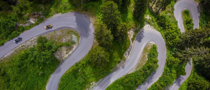 Arlberg – Dreiländereck © Moppetfoto.de Luftaufnahme einer kurvigen Bergstraße mit Motorrädern und grüner Vegetation