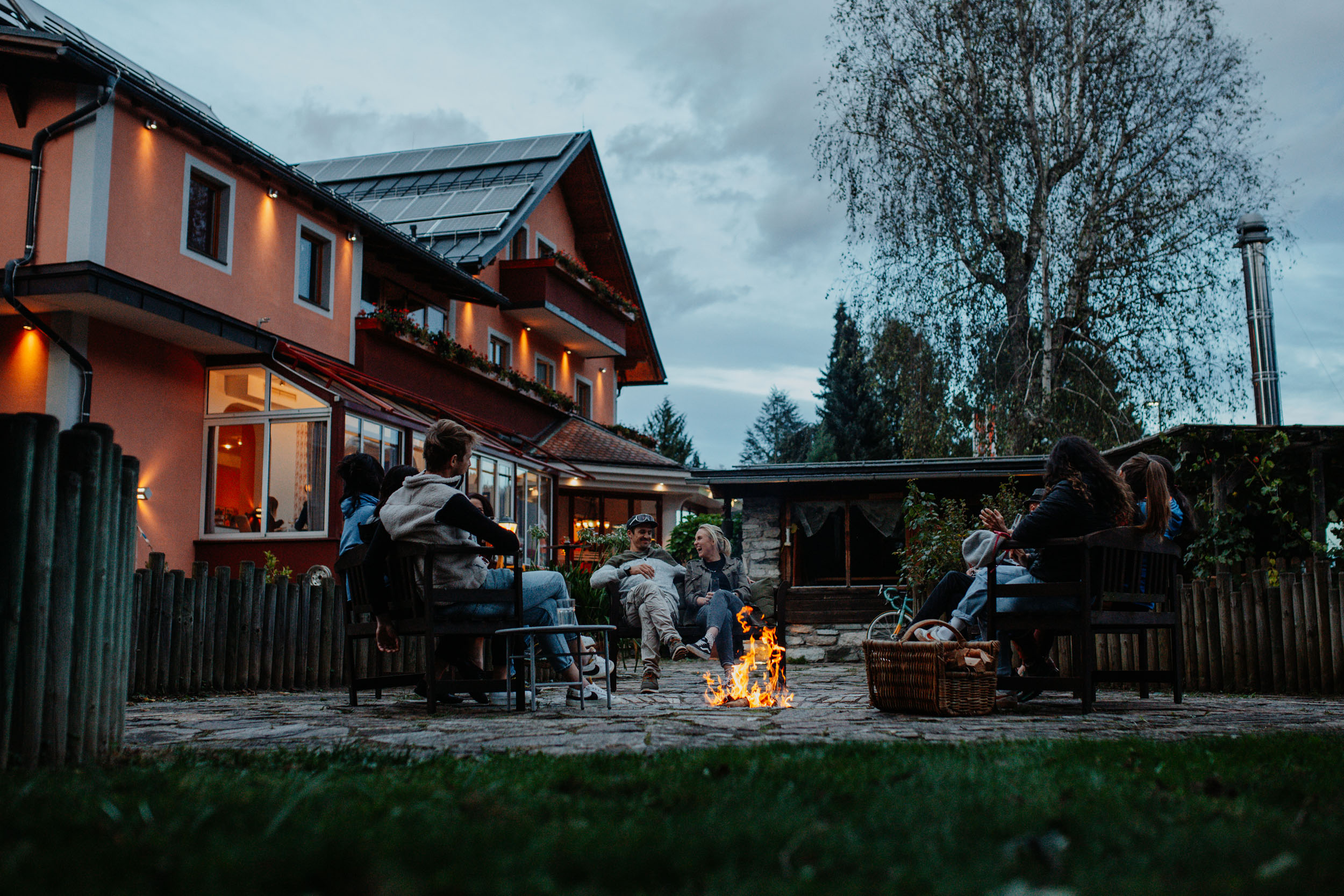 Gruppe von Menschen sitzt abends um ein Lagerfeuer im Garten eines Hauses