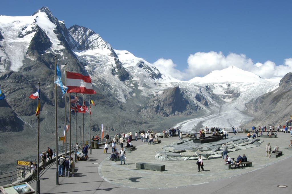 Besucher bei der Gletscherausstellung mit Alpenbergen und Gletscher im Hintergrund