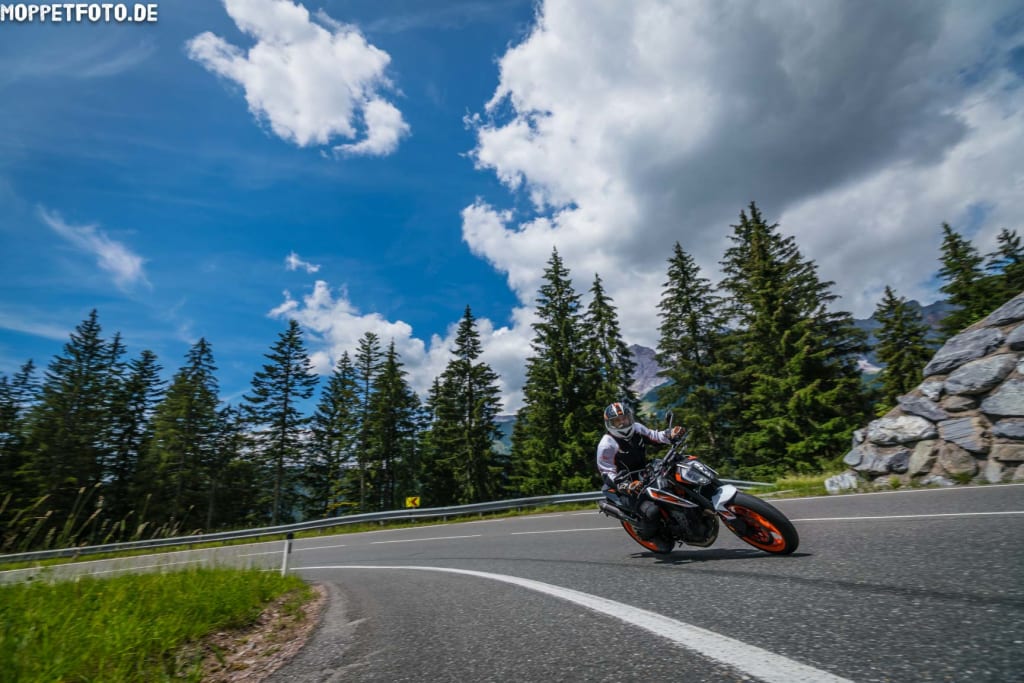Motorradfahrer fährt auf kurviger Bergstraße bei sonnigem Wetter