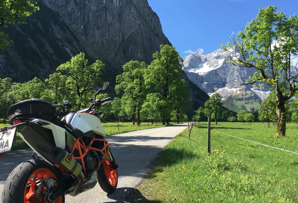 Motorrad an Landstraße mit grünen Bäumen und Bergen im Hintergrund