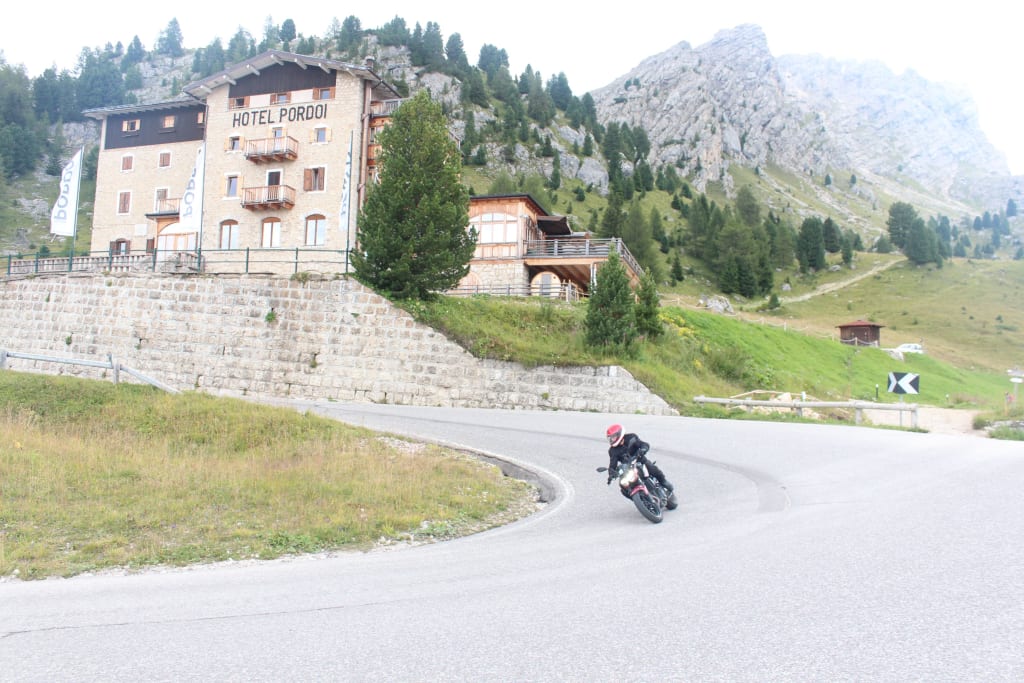 Motorradfahrer auf kurviger Straße vor Hotel Pordoi in den Bergen