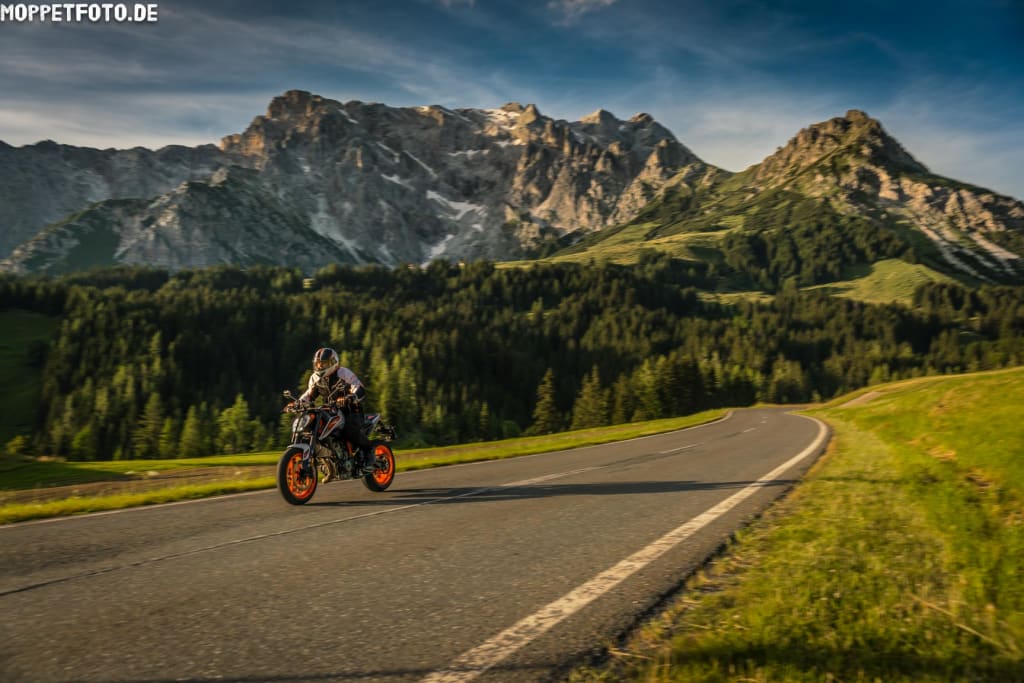 Motorradfahrer auf Bergstraße vor Felsen und Wald