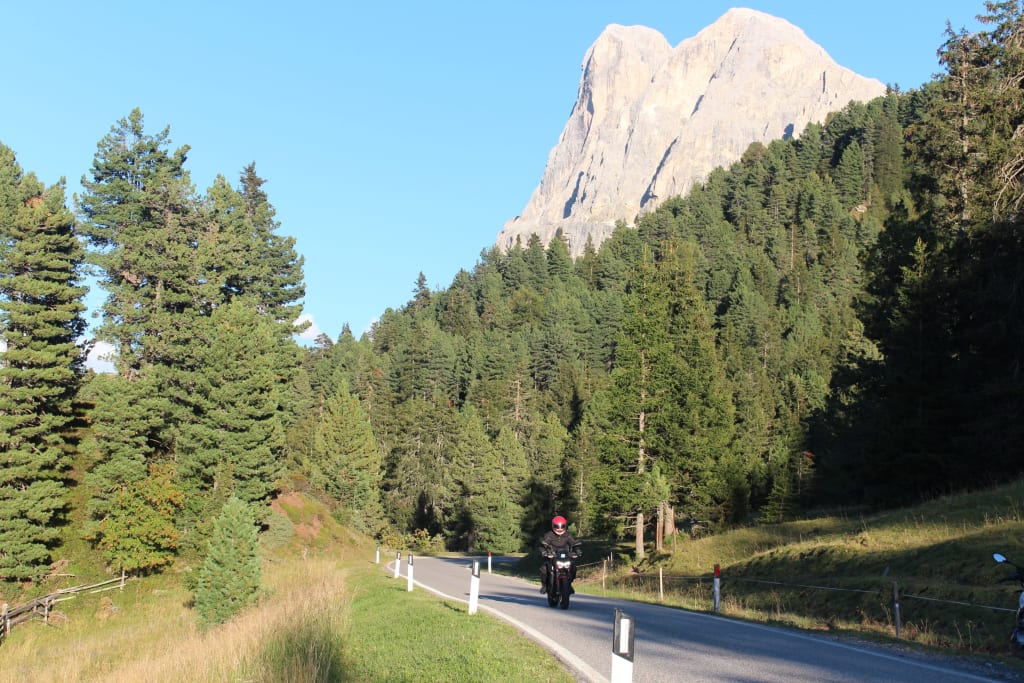 Motorradfahrer auf Bergstraße mit Tannen und Felsen im Hintergrund