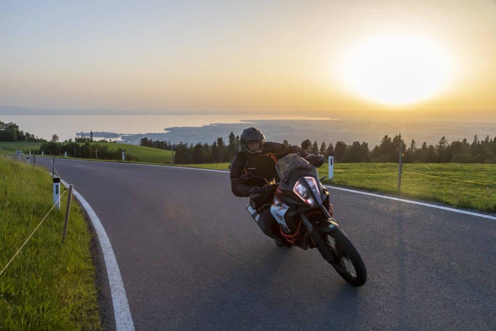 Allgäu Trip Motorradfahrer fährt auf Landstraße bei Sonnenuntergang