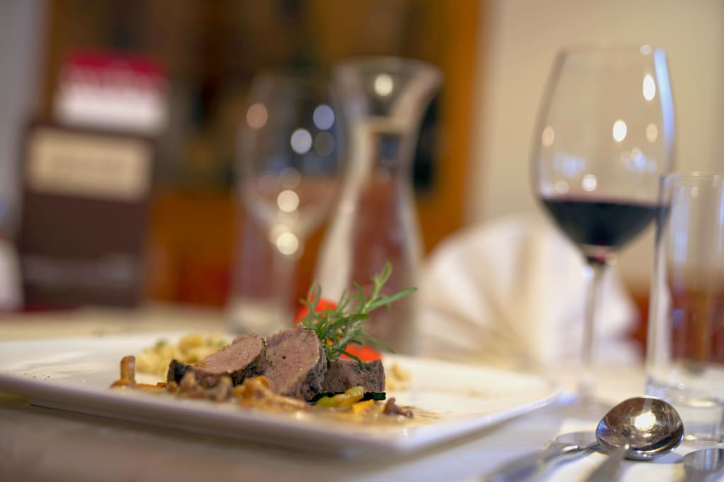 Gedeckter Tisch mit Fleisch, Wein und Besteck in einem Restaurant.