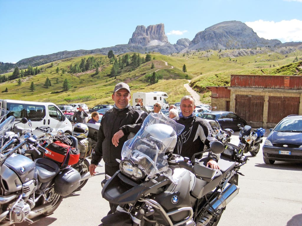 Kurvenkönig Special ab € 208,- pro Person Zwei Motorradfahrer vor Berglandschaft und Motorrädern bei sonnigem Wetter