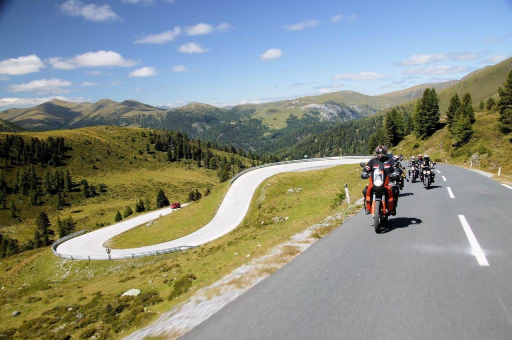 Motorradfahrer fahren auf kurviger Bergstraße unter blauem Himmel