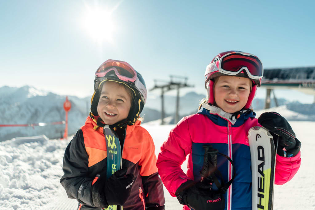 Zwei lächelnde Kinder in Skiausrüstung im Schnee am sonnigen Berg