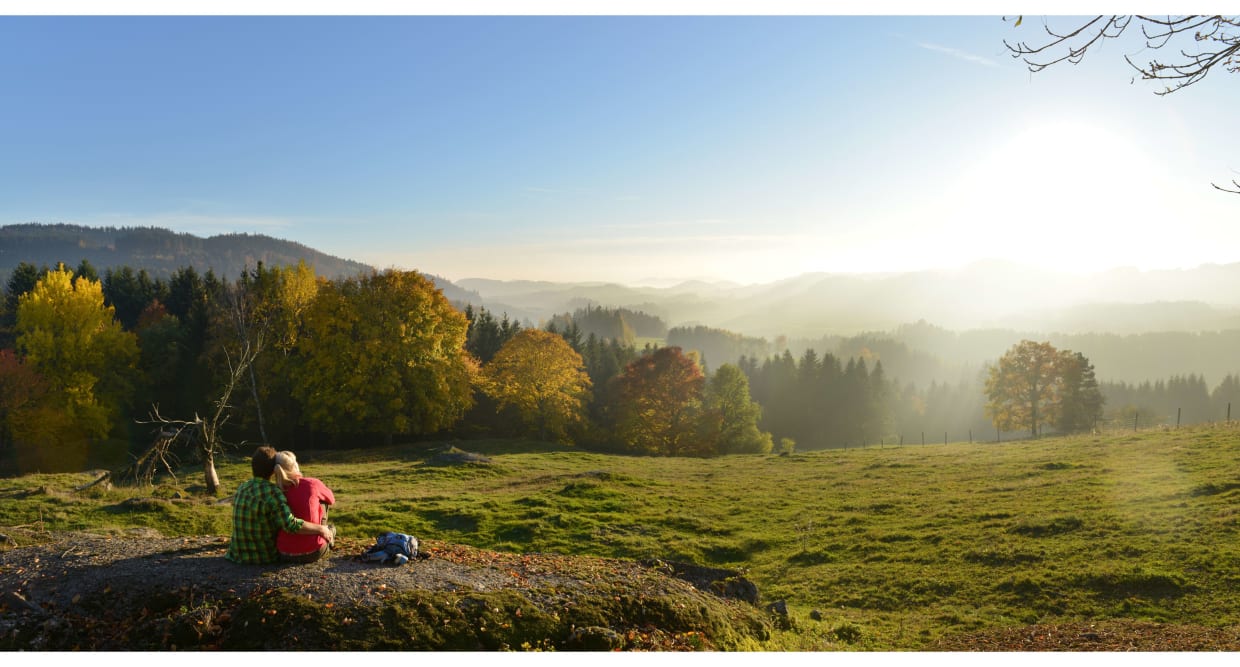Paar sitzt auf Felsen und genießt sonnige Herbstlandschaft mit Bergen