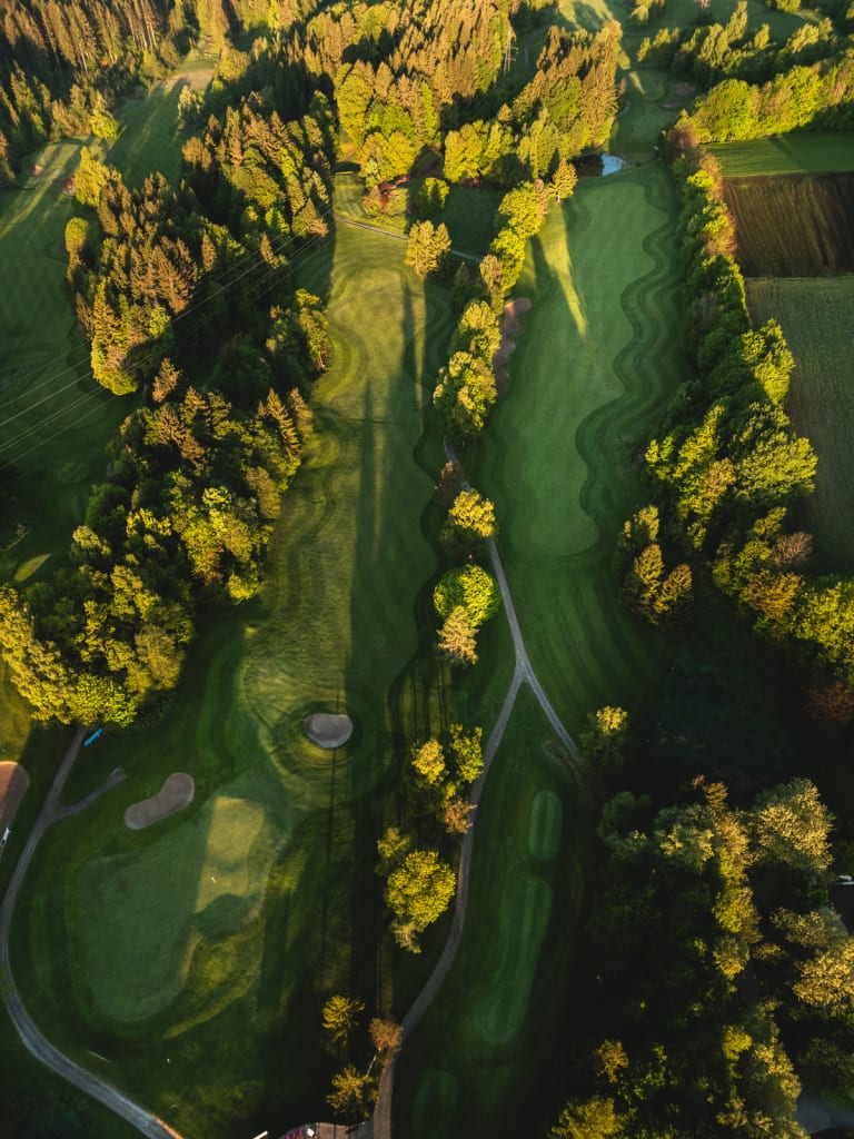 Golfwoche Luftaufnahme eines Golfplatzes mit Bäumen und langen Schatten bei Sonnenuntergang