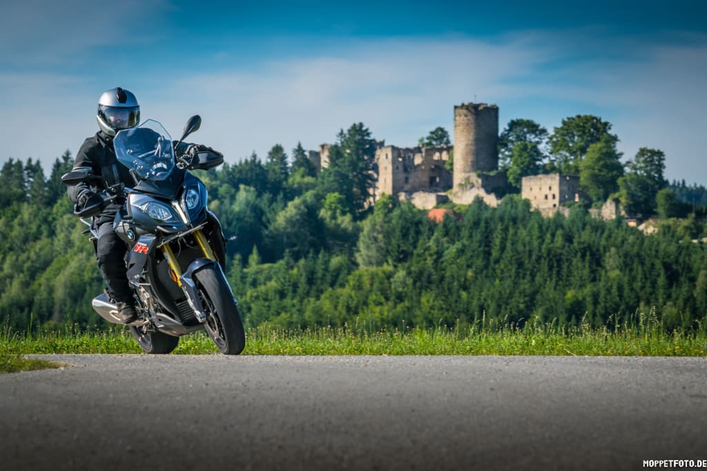 Motorradfahrer auf Landstraße vor Burgruine und Wald