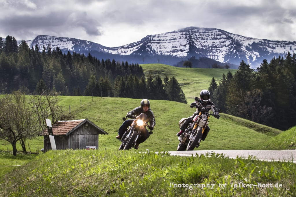 Kurvenwoche im Bergblick Zwei Motorradfahrer fahren auf Landstraße vor Alpen mit Gras und Wald