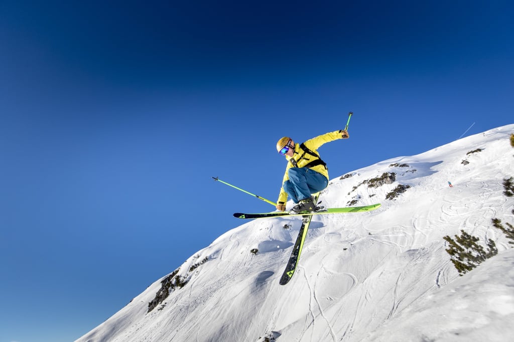 Skifahrer in gelber Jacke macht Sprung an verschneitem Berg bei klarem Himmel