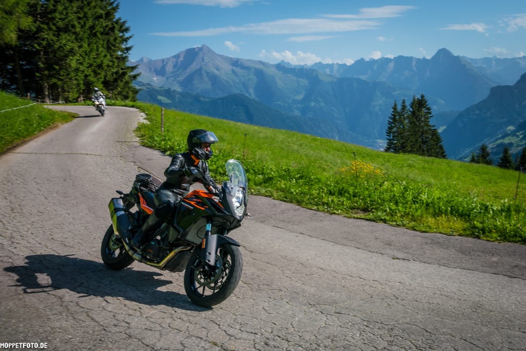 Motorradfahrer fährt auf bergiger Straße mit Blick auf Alpen
