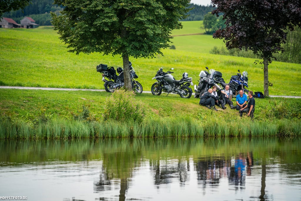 Motorradfahrer machen Pause an einem See auf einer grünen Wiese