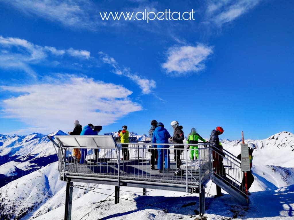 Aussichtsplattform mit Menschen und verschneiten Bergen bei klarem Himmel
