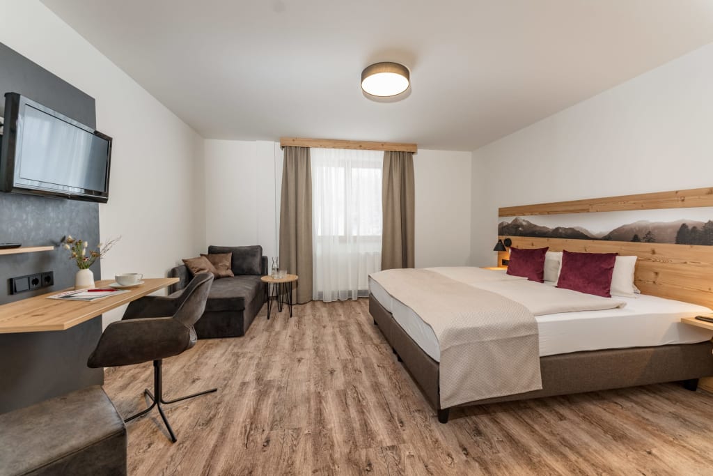Modernes Hotelzimmer mit Doppelbett, Fernseher, Tisch und gemütlicher Sitzecke
