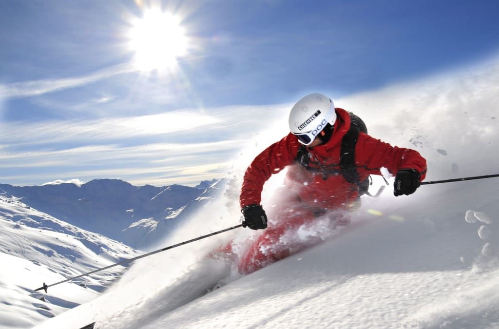Skifahrer in roter Jacke fährt schnell im Pulverschnee in den Bergen