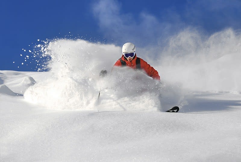 Skifahrer fährt im Pulverschnee bei blauem Himmel