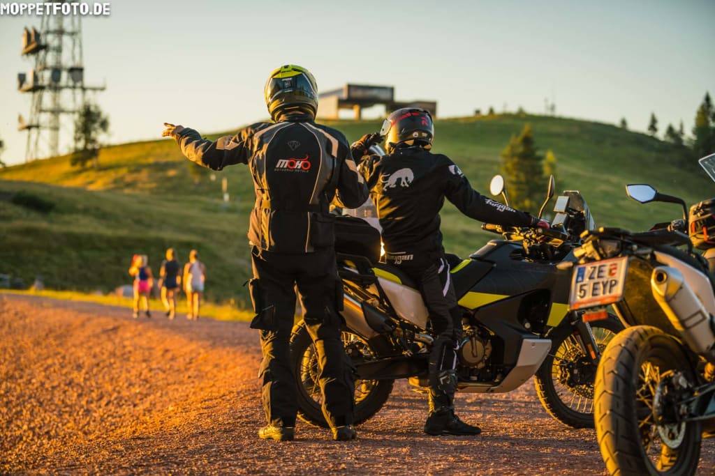 Zwei Motorradfahrer in Schutzkleidung beraten sich auf einem Landweg bei Sonnenuntergang